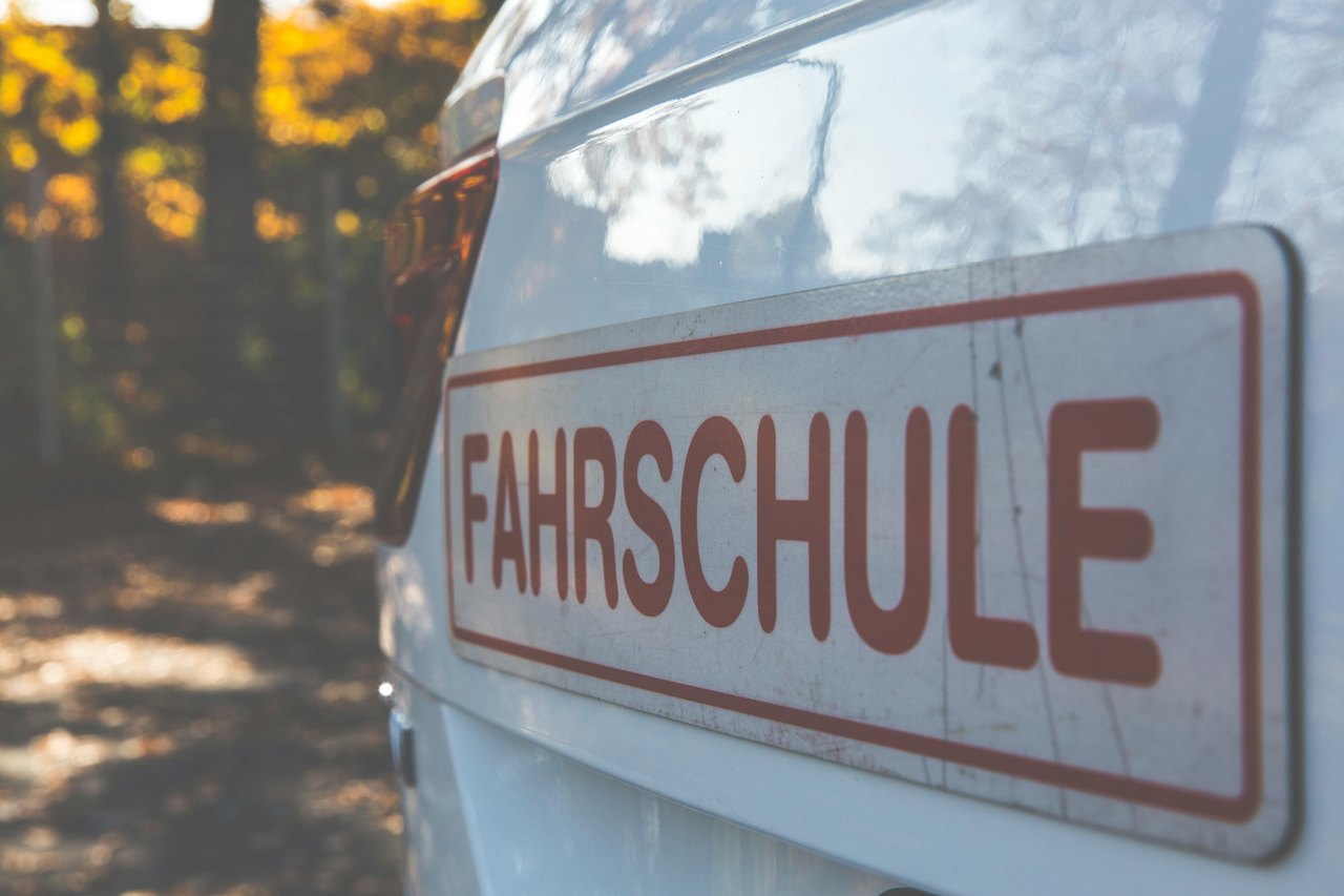 Heck eines weißen Autos mit rotem Schild "FAHRSCHULE" darauf.