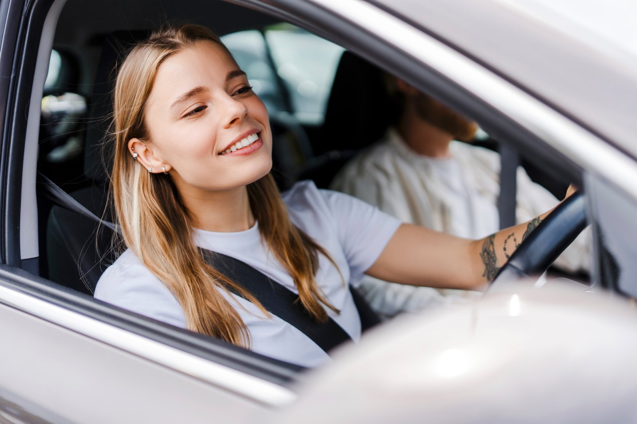 Lächelnde junge blonde Frau fährt Auto, angeschnallt.
