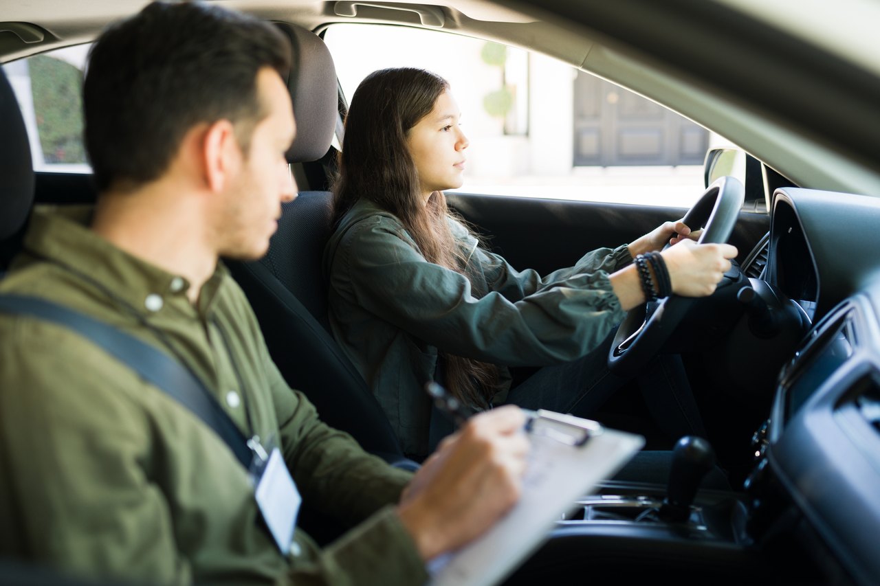 Fahrlehrer beobachtet eine junge Frau am Steuer während einer Fahrstunde.